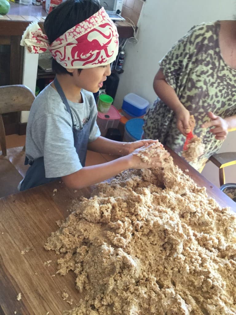 Anak dan orang dewasa menyiapkan miso dalam jumlah besar di meja kayu